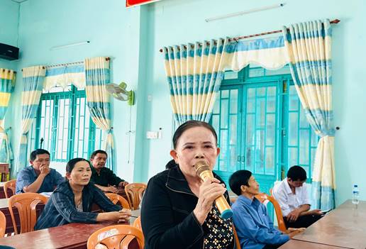 Description: A person holding a microphone in front of a group of people sitting at a table  Description automatically generated